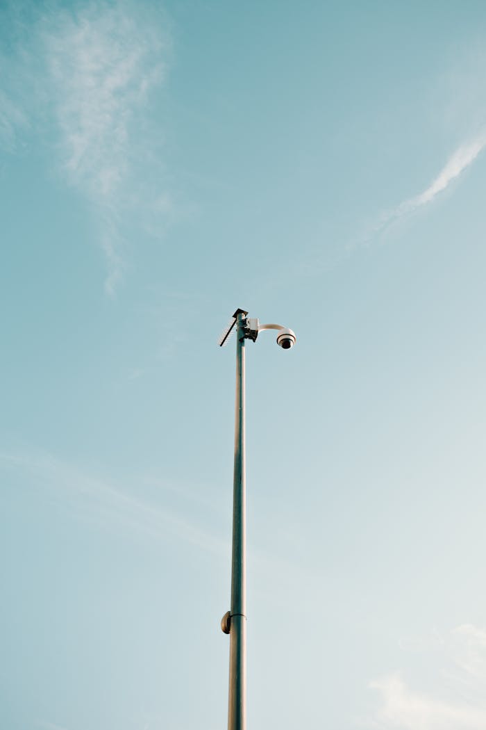 From below of contemporary security camera placing on top of high pillar in city under clear blue sky